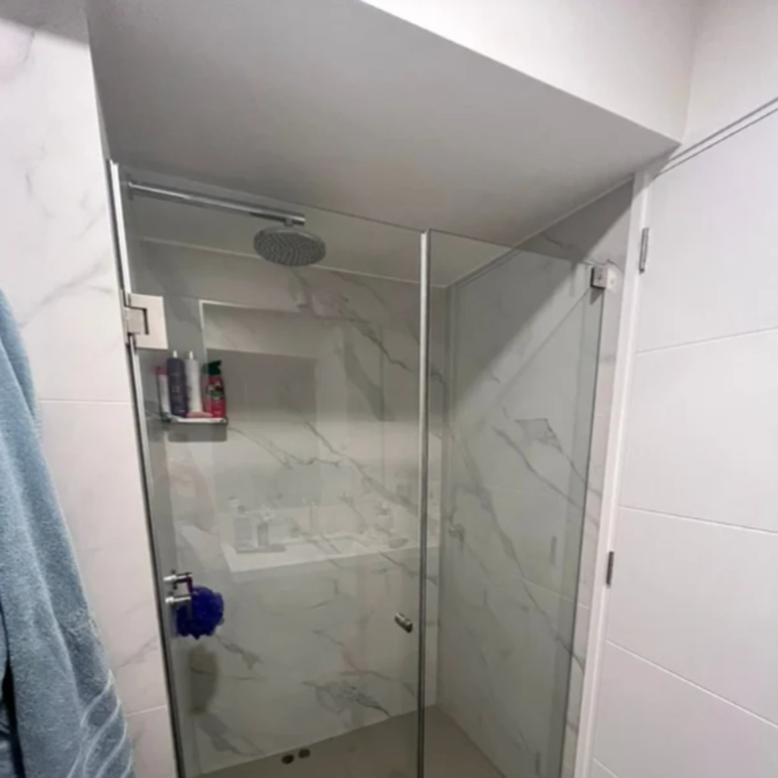Mampara batiente de vidrio templado en una ducha con revestimiento marmoleado