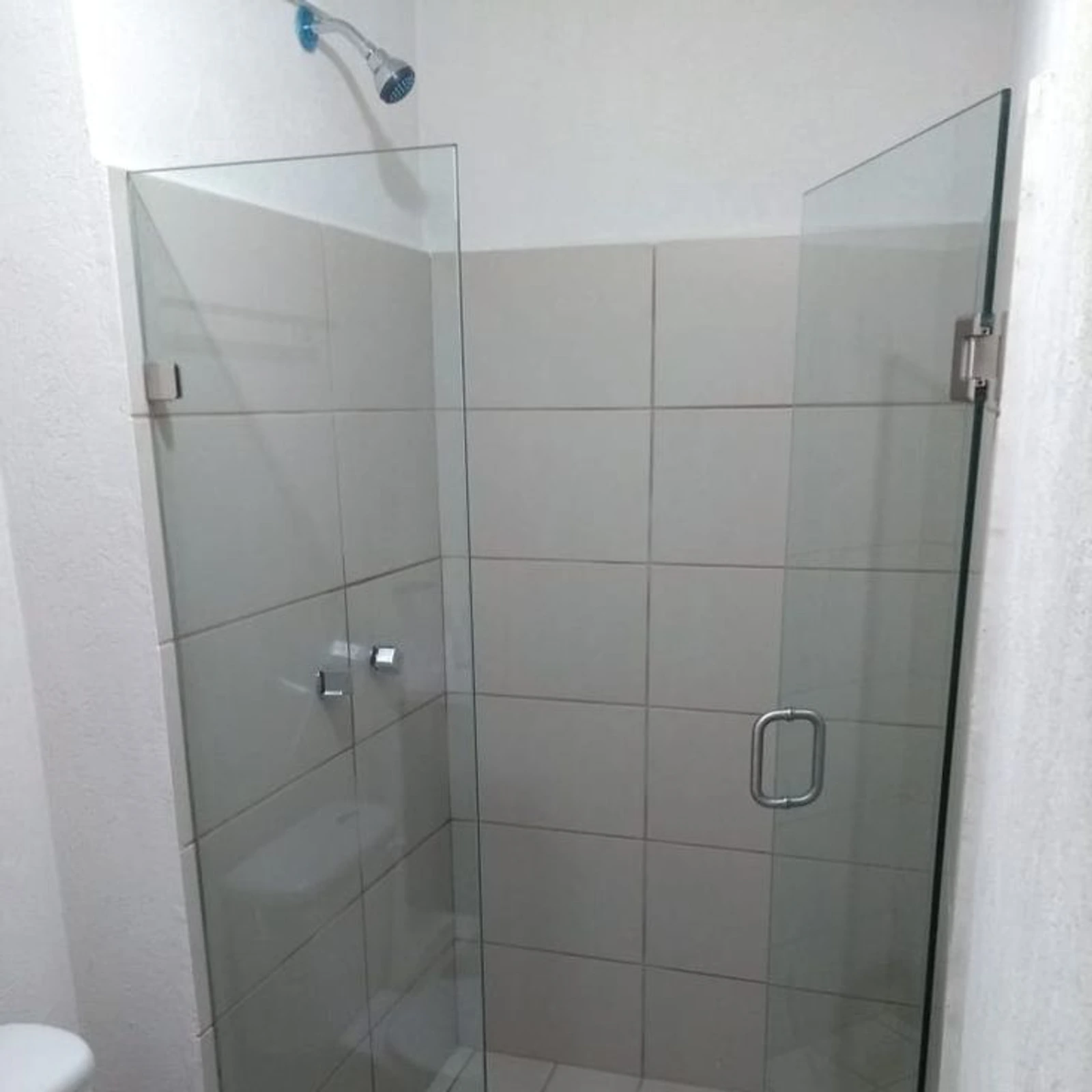 Mampara batiente de vidrio templado con jalador, en una ducha alicatada en blanco