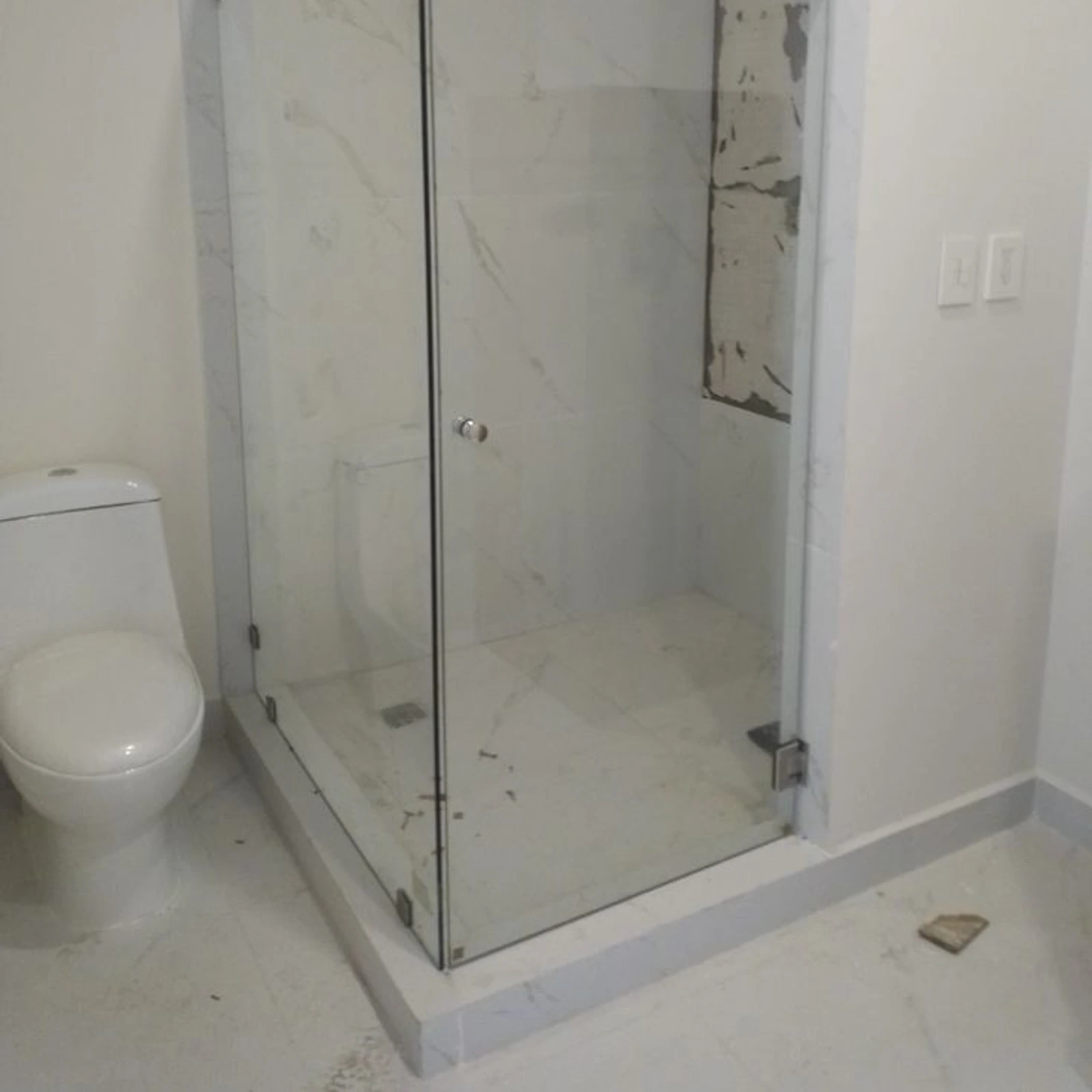 Mampara batiente esquinera de vidrio templado en un baño de revestimiento marmoleado
