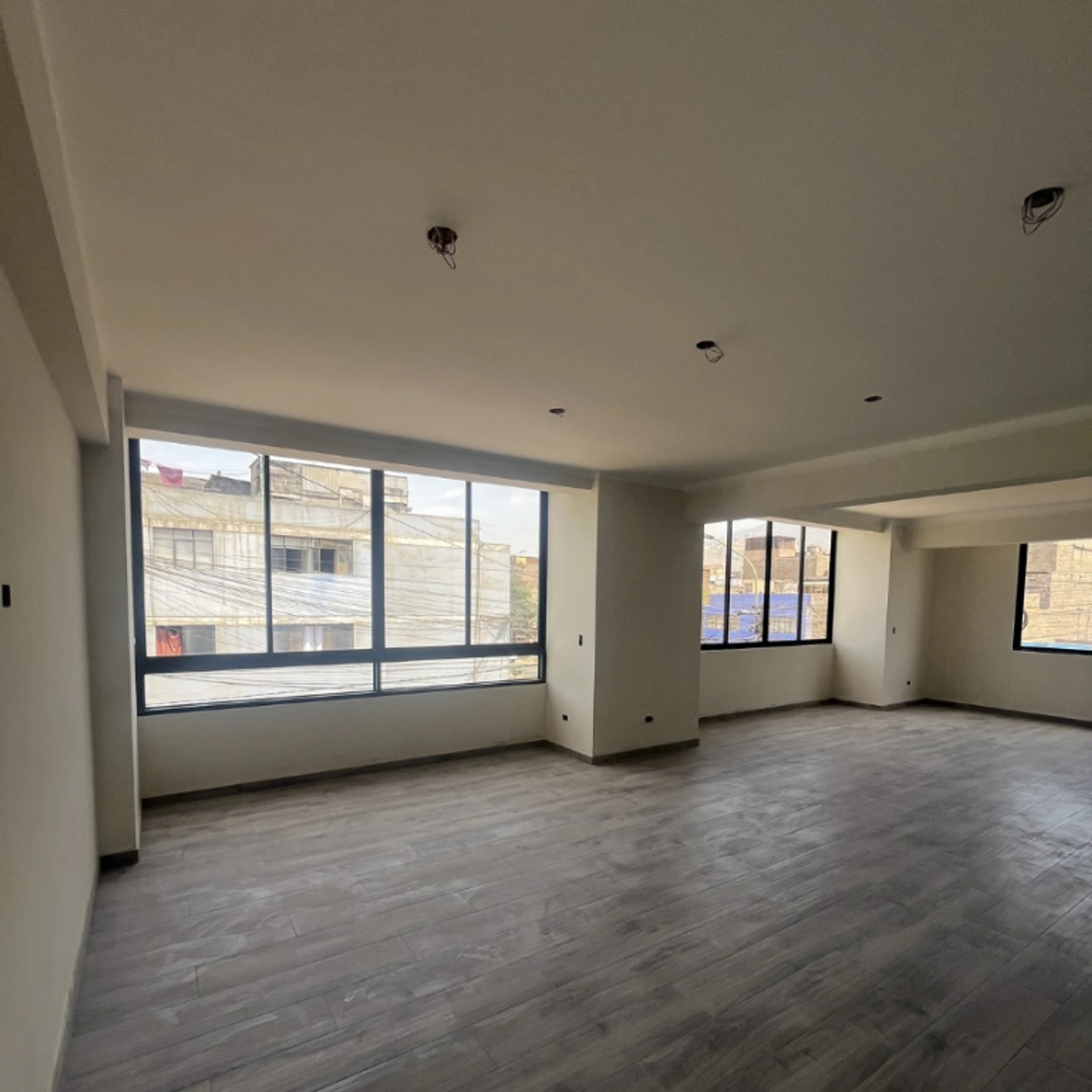 Sala vacía con dos ventanas corredizas de perfilería negra y piso de madera