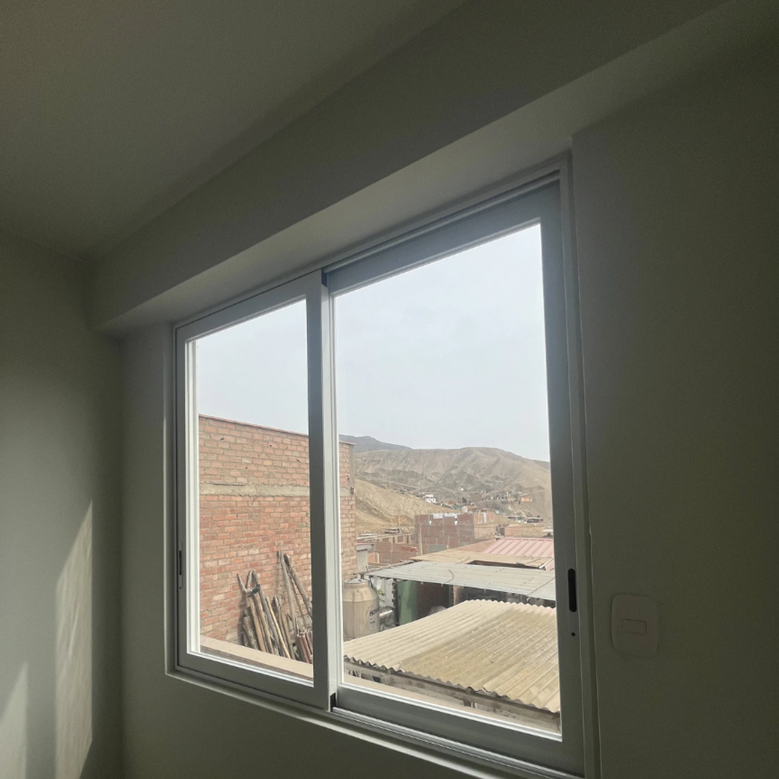 Ventana corrediza de dos hojas con perfilería blanca y vista al cerro