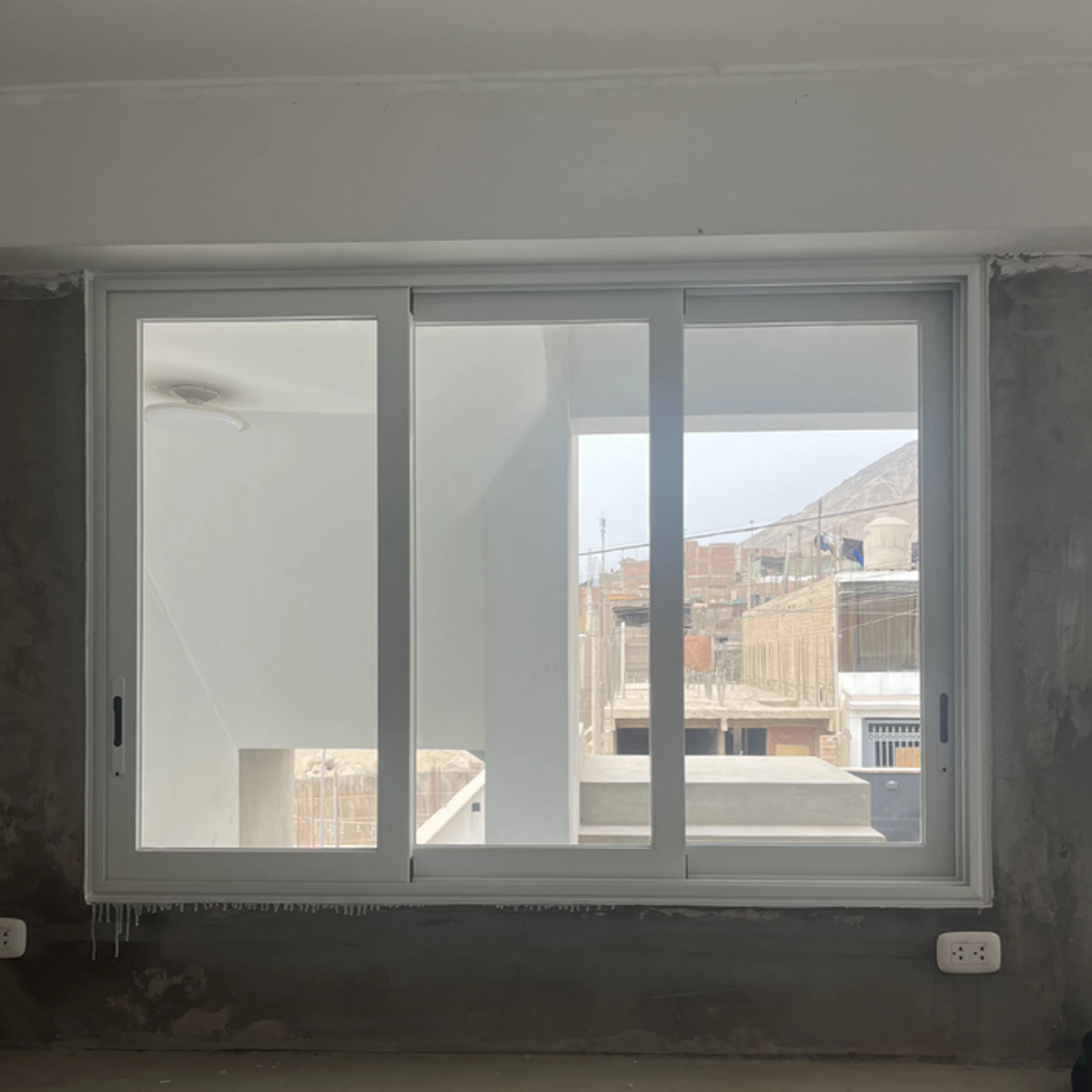 Ventana corrediza de perfilería blanca en un ambiente en obra gris