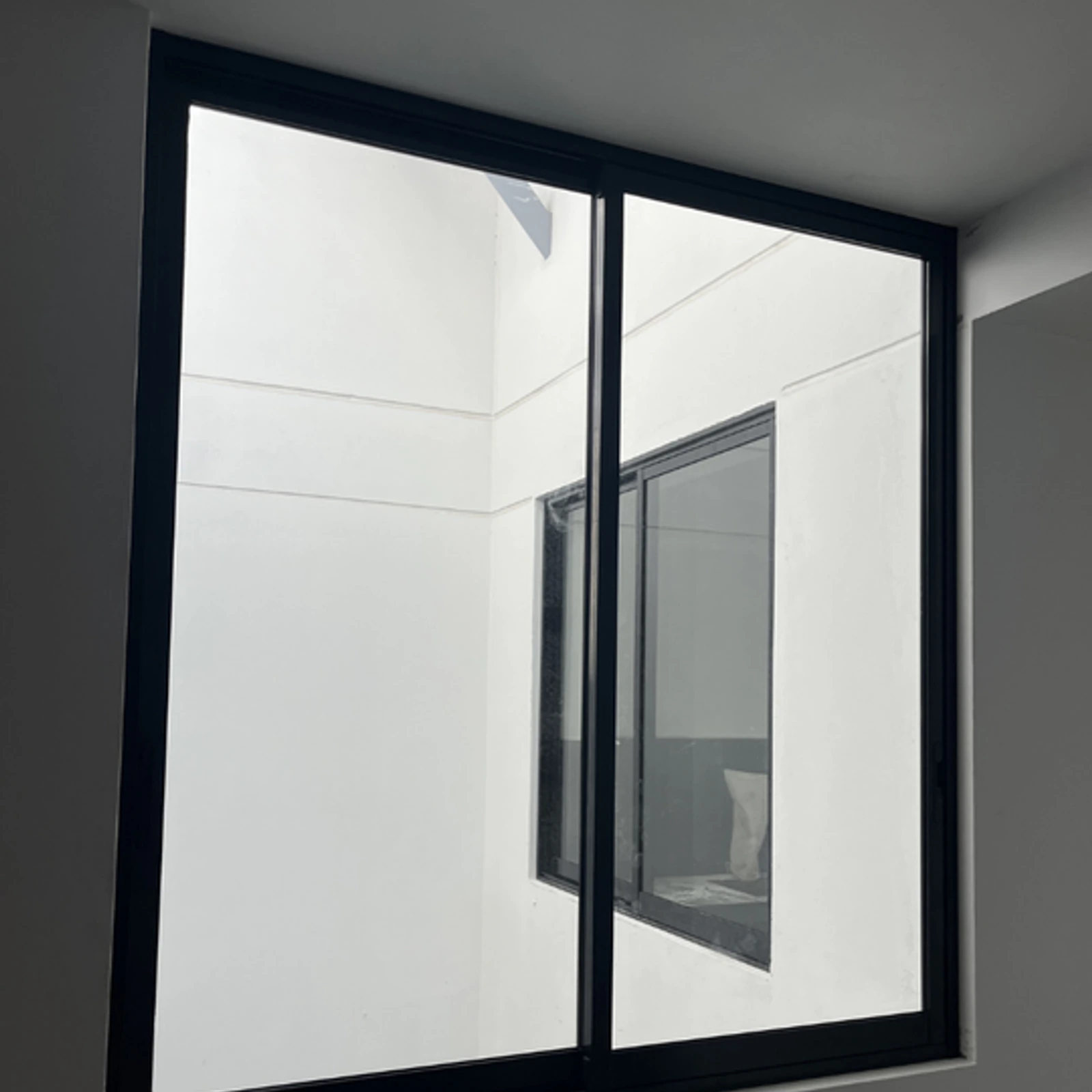 Ventana corrediza de dos hojas con perfilería negra que da a un patio de luz interior