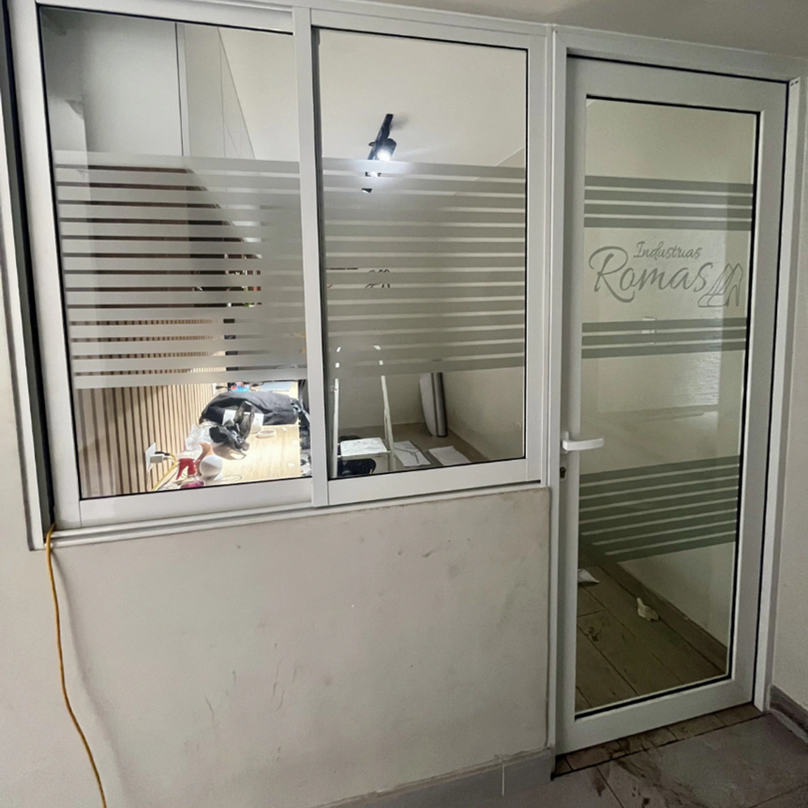 Ventana y puerta de aluminio blanco con vinilo esmerilado a franjas en la entrada de una oficina