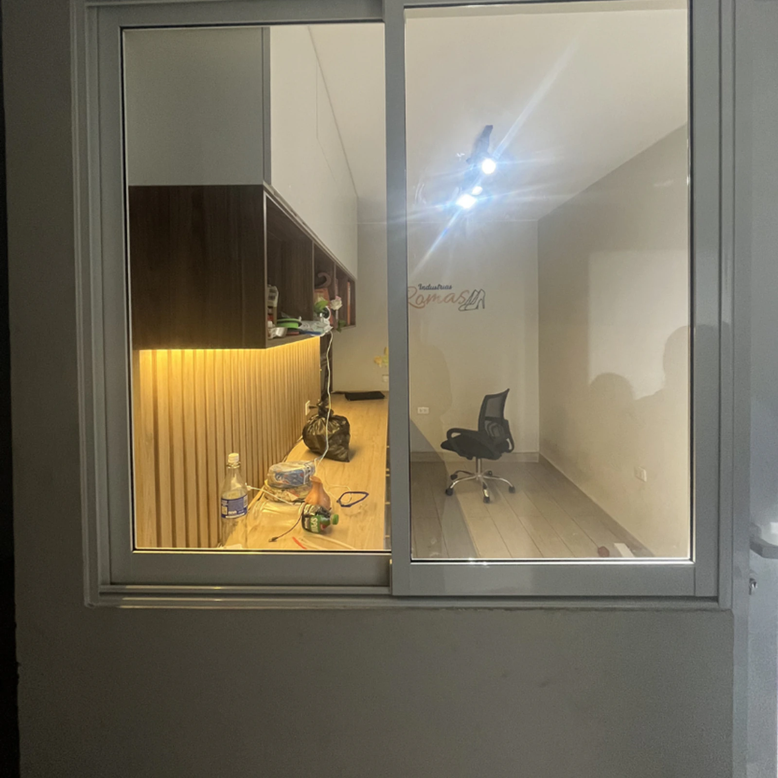 Ventana corrediza de aluminio blanco vista desde fuera, con una oficina iluminada al fondo