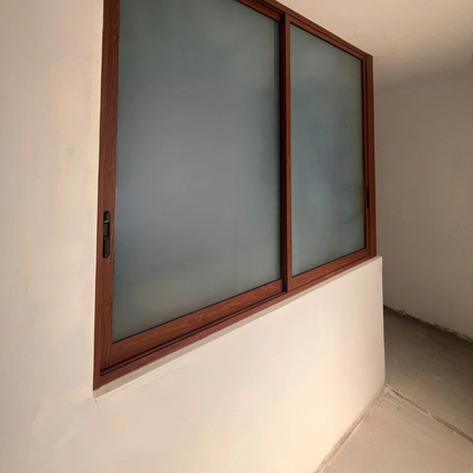 Ventana corrediza de perfilería color madera con vidrio esmerilado, en un ambiente en obra