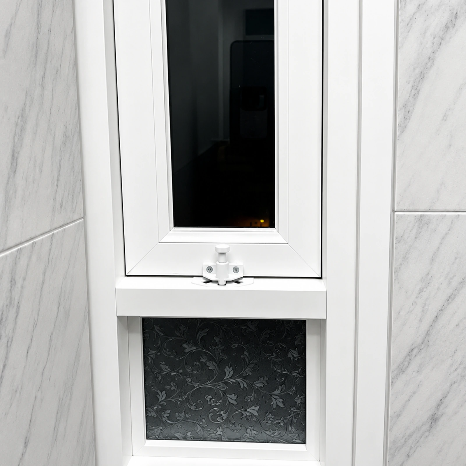 Ventana pivotante de aluminio blanco cerrada, en un baño con revestimiento tipo mármol