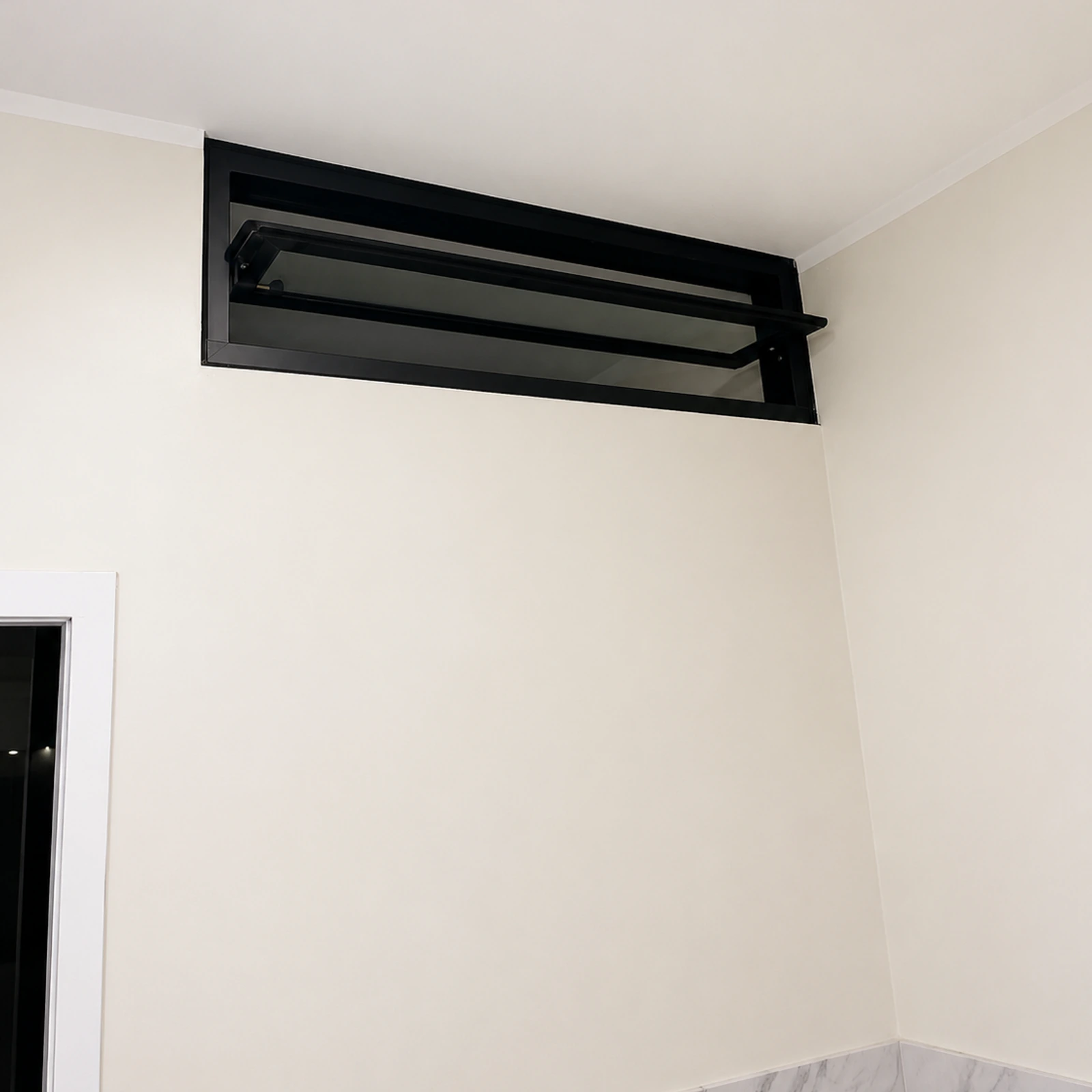 Ventana pivotante de aluminio negro instalada en la parte alta de una pared