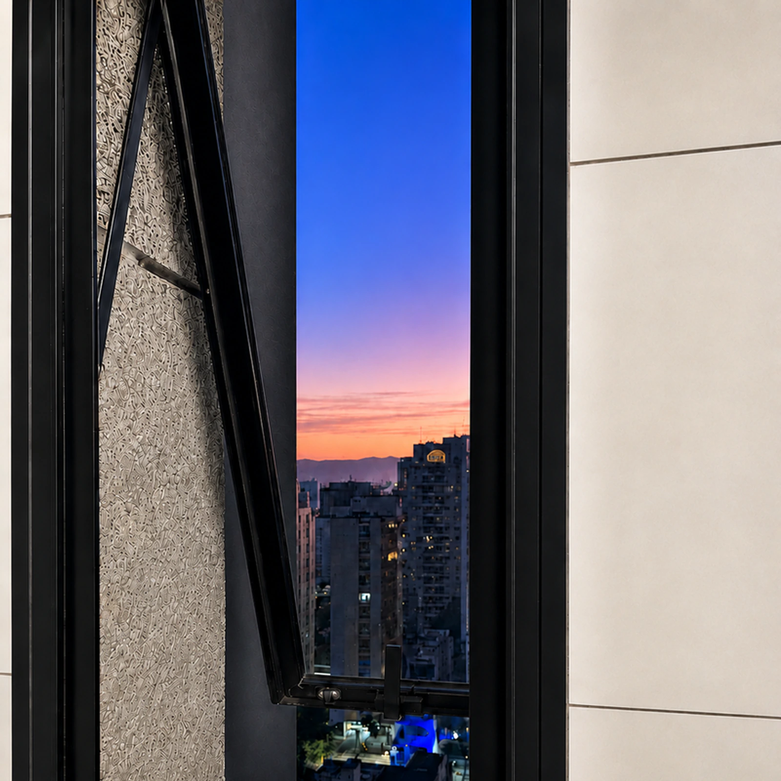 Ventana proyectante de aluminio negro abierta, con vista a la ciudad al atardecer